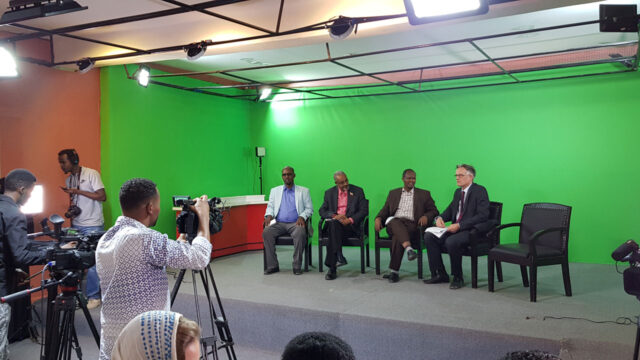 Journalism faculty members sitting in front of cameras in a green screen studio room