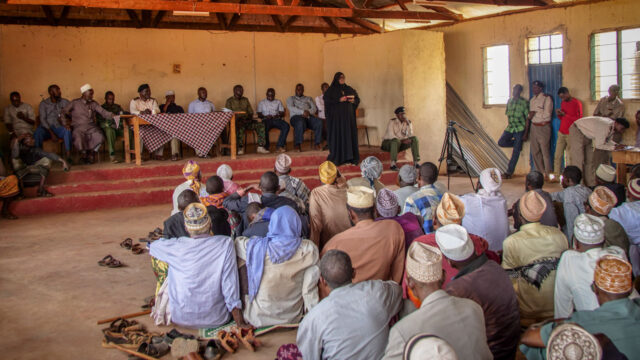 Panellists on the stage of a community centre with an audience of community members