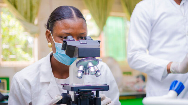 A scientist wearing a mask looking at a sample under a microscope