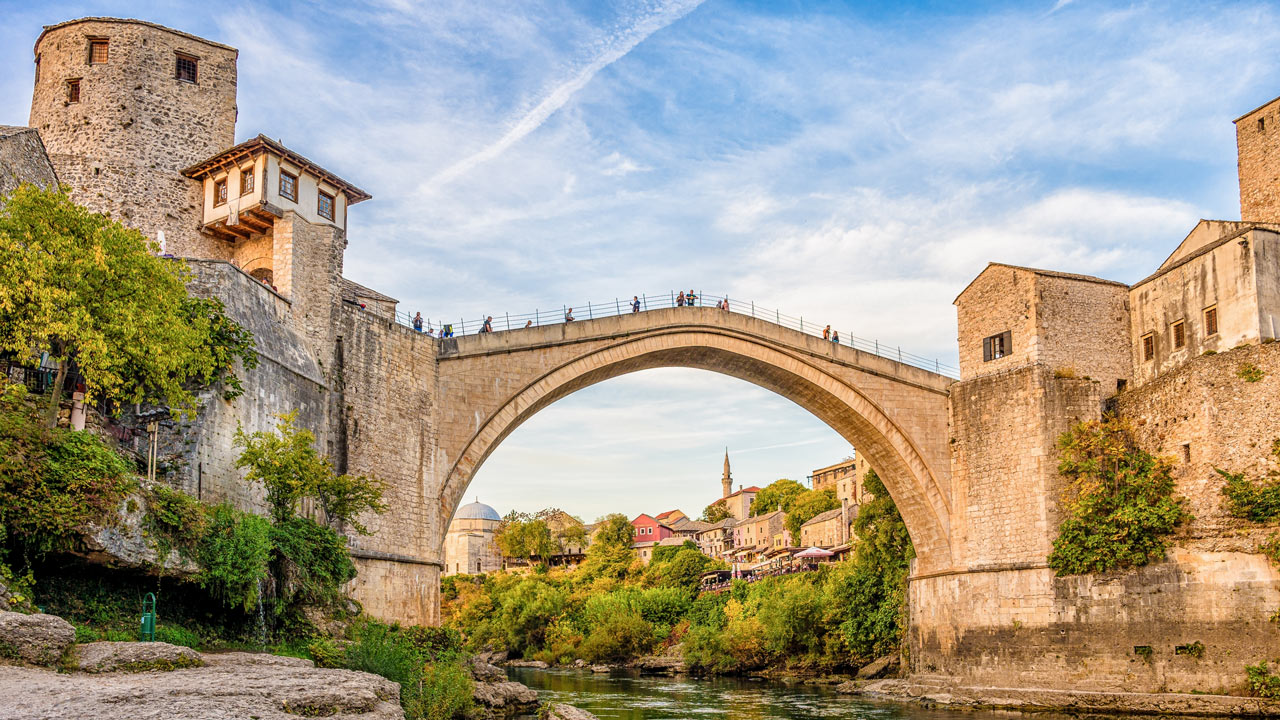 People crossing over an arced bridge through a Balkan town
