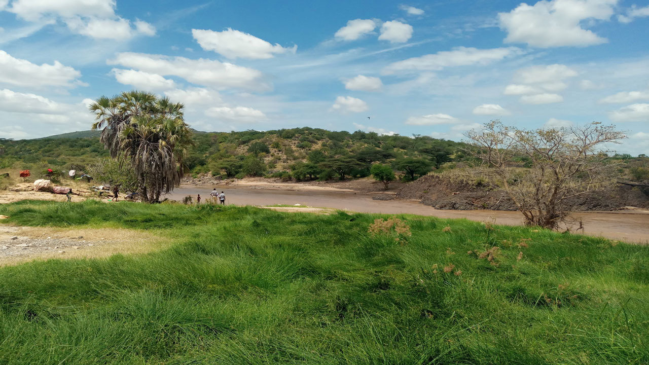 Distant people standing along the bank of a low-tide river bordered by a grassy green field