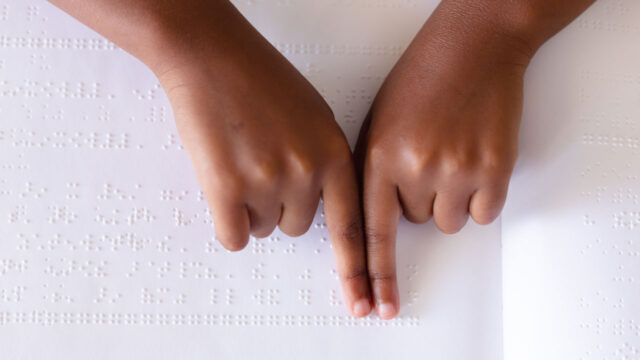 A child's hands on top of a white sheet of braille