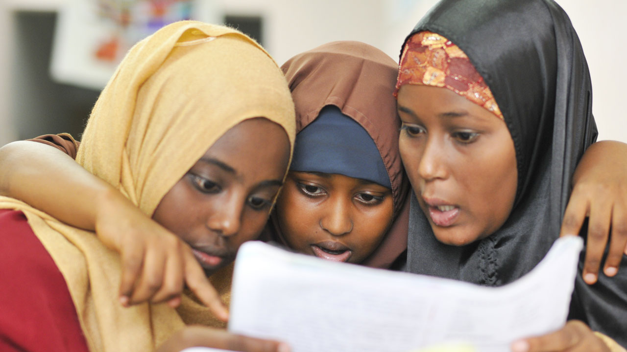 Three schoolgirls in an embrace reading a piece of paper