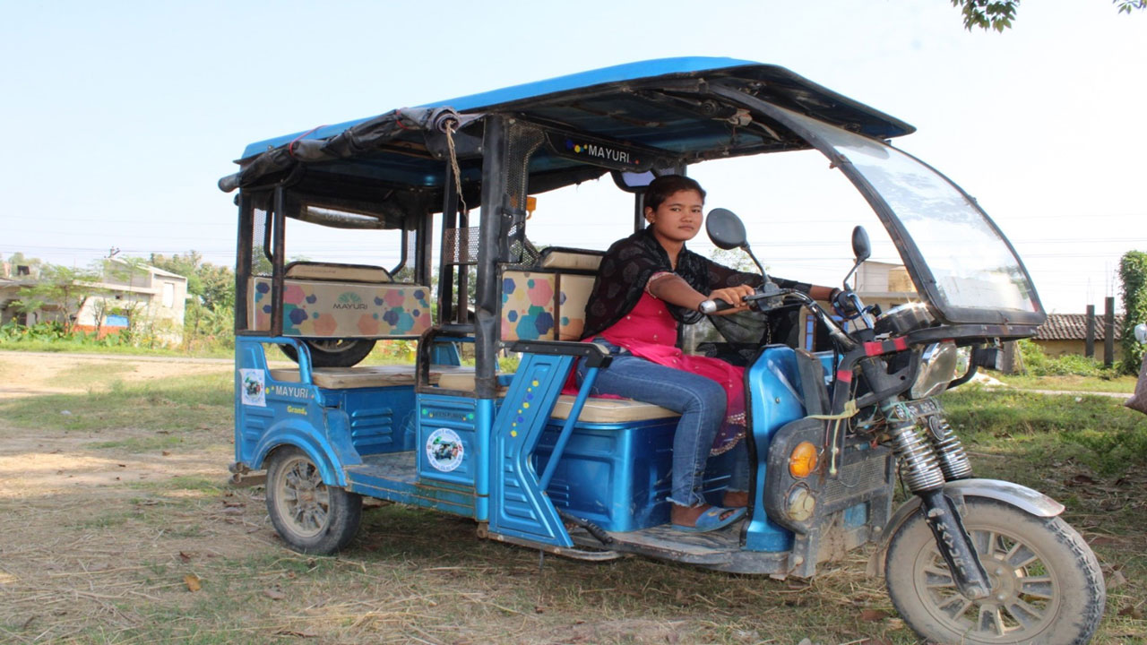A young woman driving a blue tuk-tuk vehicle