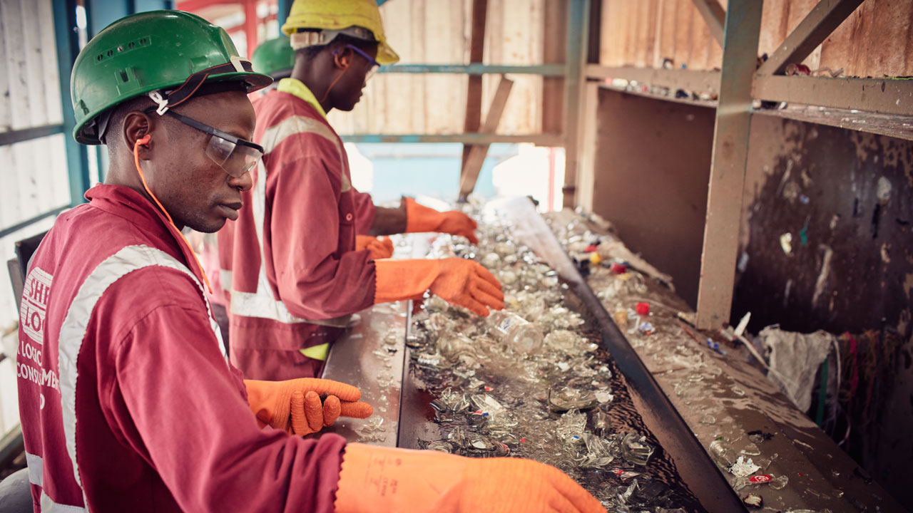 Recycling plant workers wearing protective gloves and eye protection while sorting wet broken glass on a conveyor belt