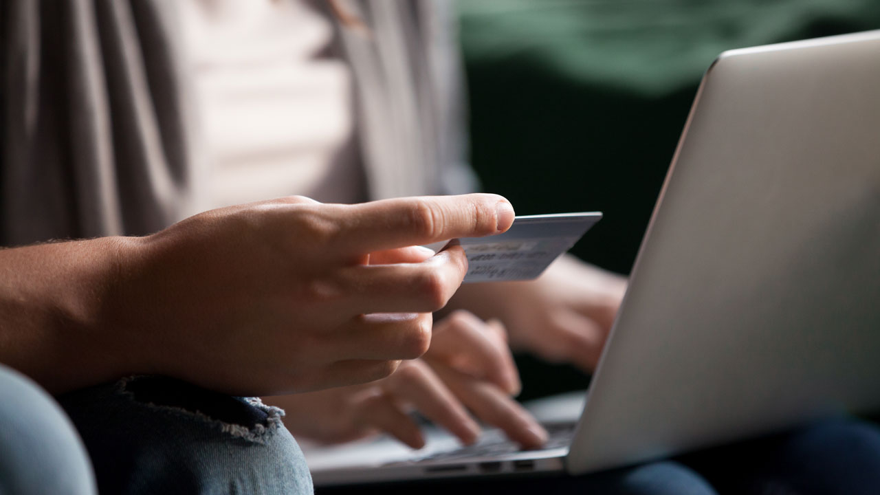 One person holding a credit card while the person sitting next to them other inputs its info on a laptop