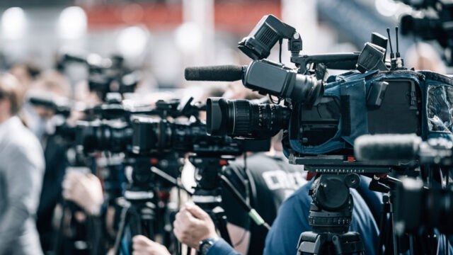 A group of news camera handlers at the front of a crowd