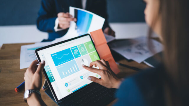 Corporate staff reviewing data on a tablet and in printed plans at a conference table