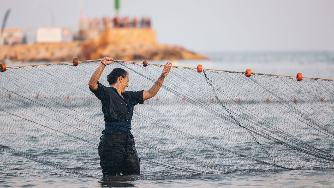 Fisher handling a fishing net while wading thigh-deep through shore water