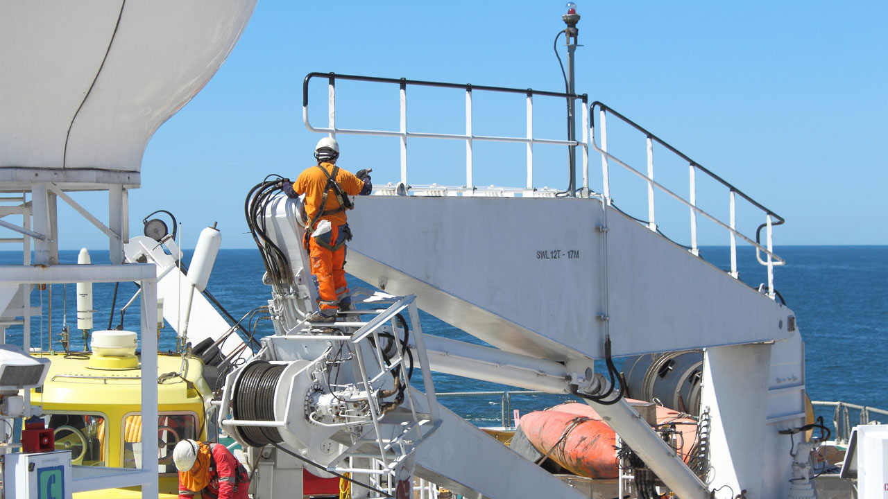 A seafarer in a hard hat and high visibility gear inspecting parts aboard a maritime transport vessel at sea