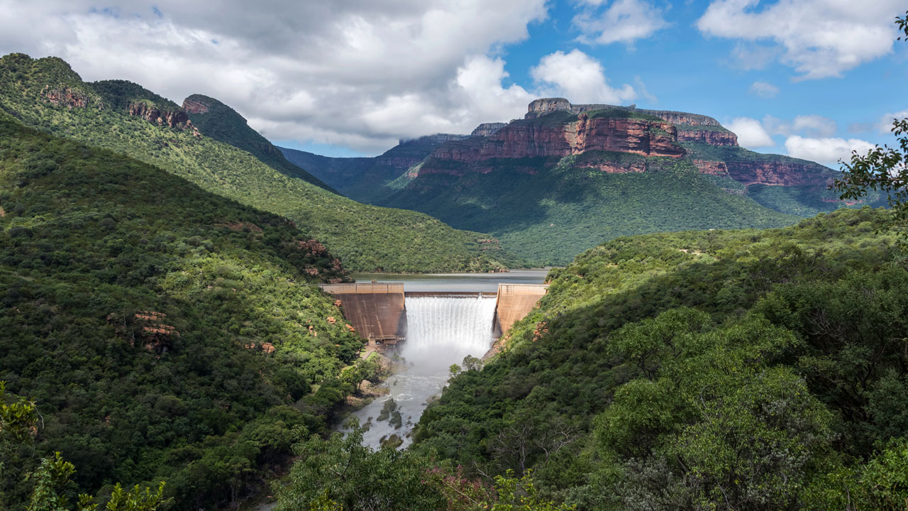 A controlled waterfall running from a dam in vegetated mountains