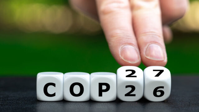 Fingers turning dice that read “COP26” into “COP27”