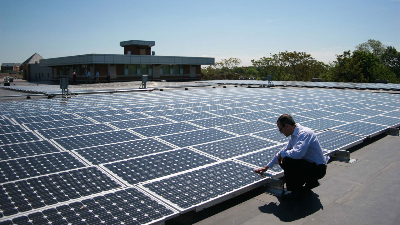 Person in business attire inspecting and crouching next to solar panels