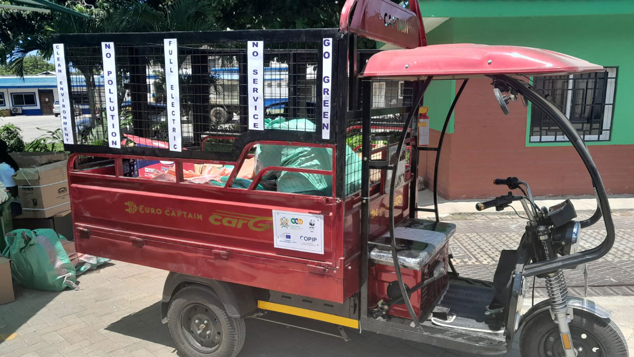 A red waste collection tuk-tuk vehicle carrying a few bags of trash in the back