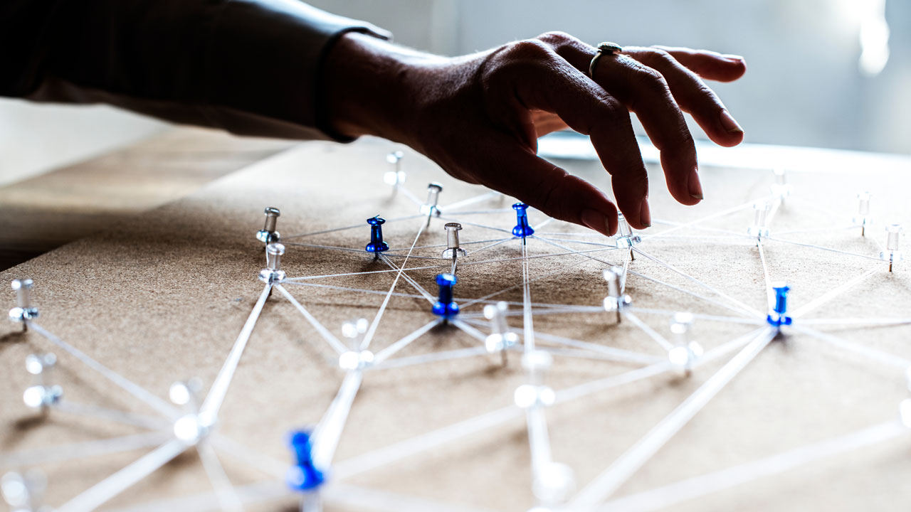 A hand placing pins connected by white strings on a board