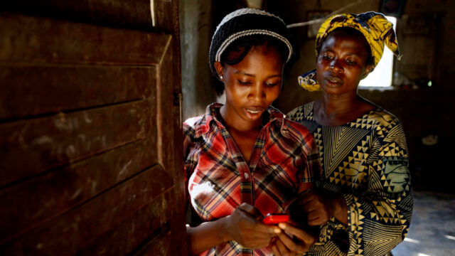 Two women standing next to a wooden door, one using a small mobile device