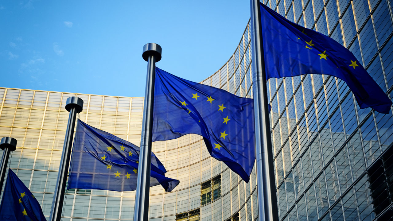 A row of European Union flags flying in front of a tall modern building