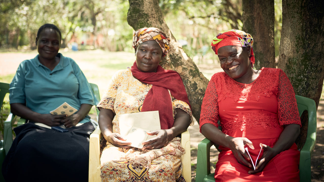 Three women with pamphlets seated at an outdoor event
