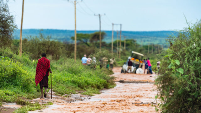 Person with a walking cane heading towards a group by a jeep in the middle of a dirt path