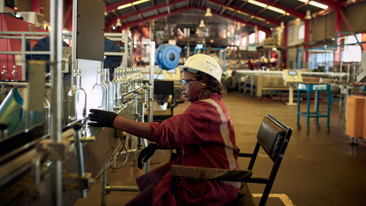 A factory worker wearing a hard hat, inspecting empty glass bottles on an assembly line