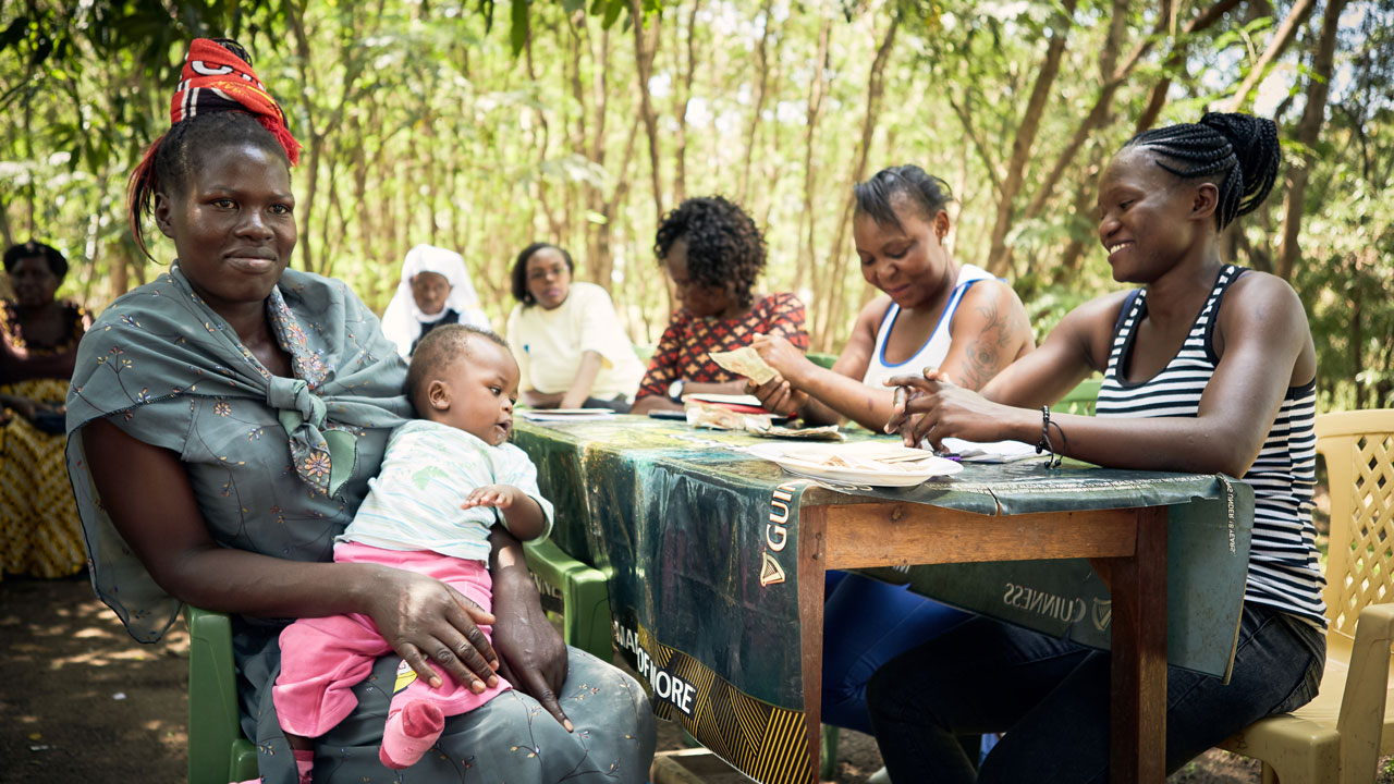 A mother with her baby sitting at an outdoor event table with coordinators sitting at the other side