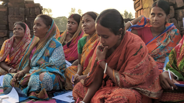 A group of women sitting on a striped blanket looking at brochures