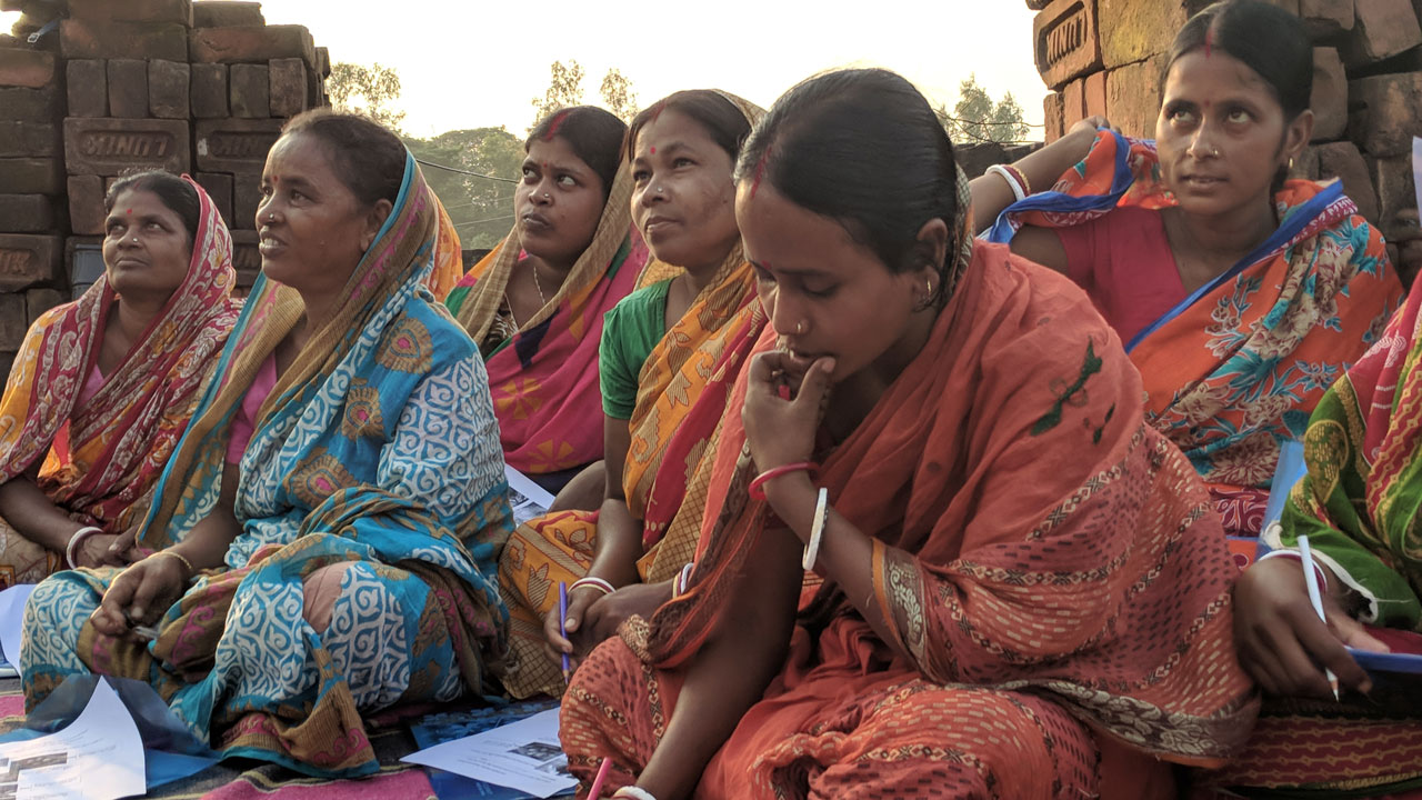 A group of women sitting on a striped blanket looking at brochures