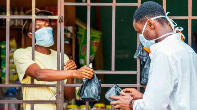Two people with masks exchanging goods through a barred storefront