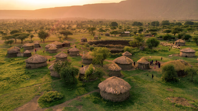 Expansive view of a pastoral mountainside Zimbabwean village tinged in orange sunlight