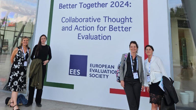 Four women posing in front of the 15th European Evaluation Society Conference sign