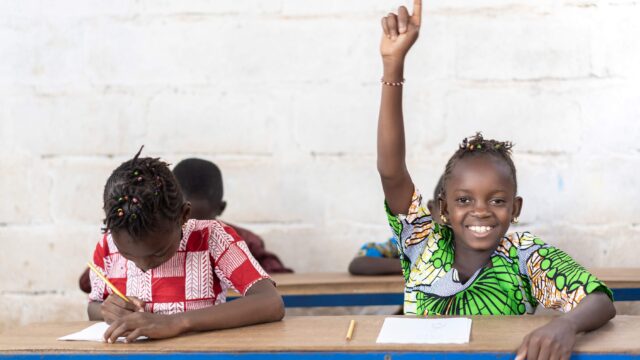 School children reading and raising their hand during the lesson