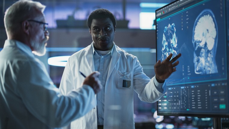 A scientist and a surgeon discussing MRI brain scan on TV display.